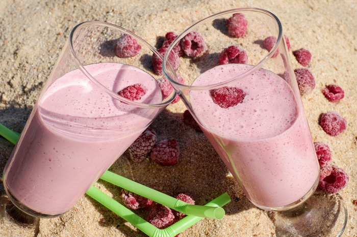 Two raspberry cocktails on sand with raspberries