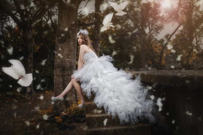 Woman in white dress with doves in forest