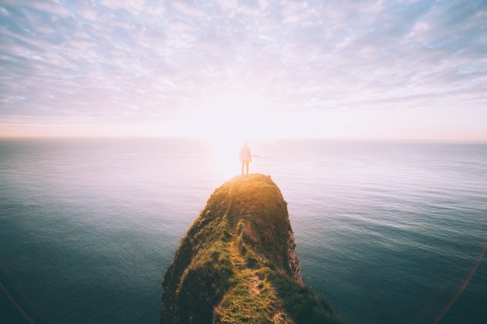 Person standing on a cliff overlooking the sea at sunrise