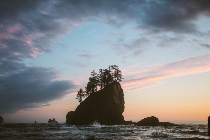 Rock formation with trees in the ocean at sunset