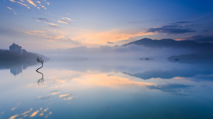 Misty lake at sunrise with mountains and a lone tree