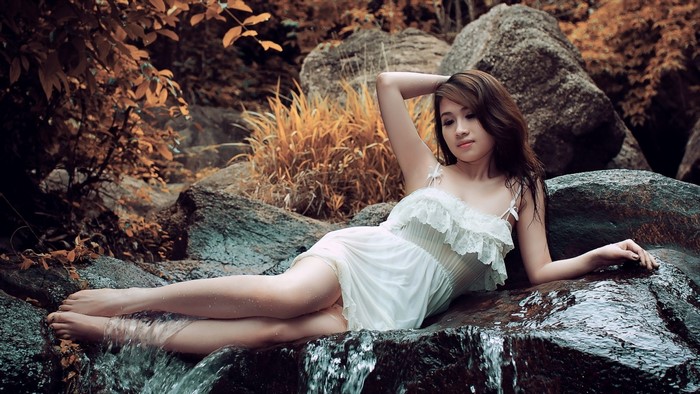 Woman Relaxing on Rocks with Flowing Water in Forest