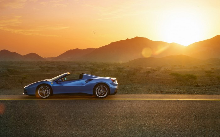 Blue Ferrari convertible driving on a road at sunset