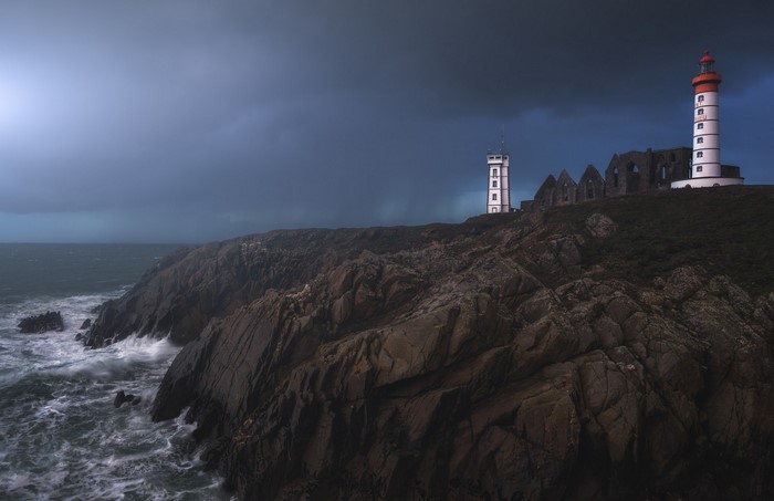 Lighthouse and ruins on a rocky coast during a storm