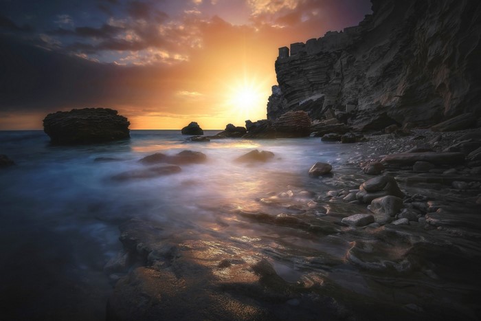Sunset Over Rocky Coastal Bay with Misty Waters