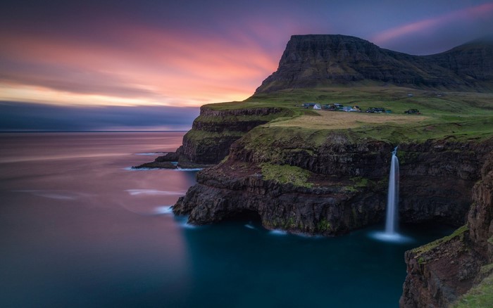 Waterfall cascading from cliffs into the sea at sunset