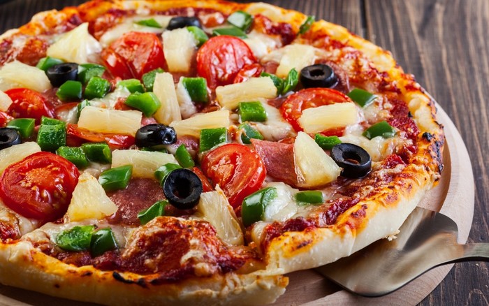 Close-up of a delicious Hawaiian pizza with pineapple, tomatoes, and olives
