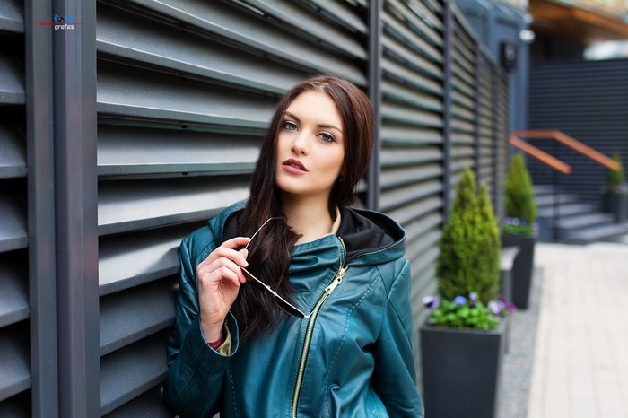 Woman in teal jacket holding sunglasses