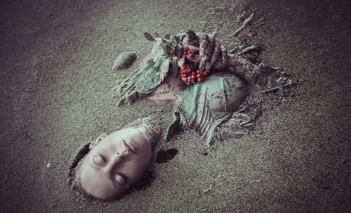 Woman buried in sand with berries and leaves