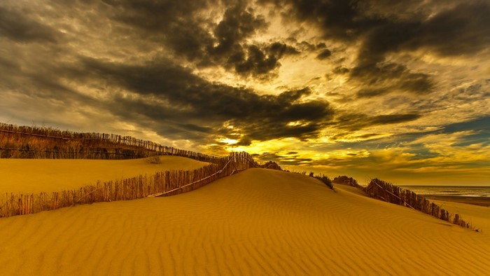 Sand dunes with wooden fences under a dramatic sunset sky