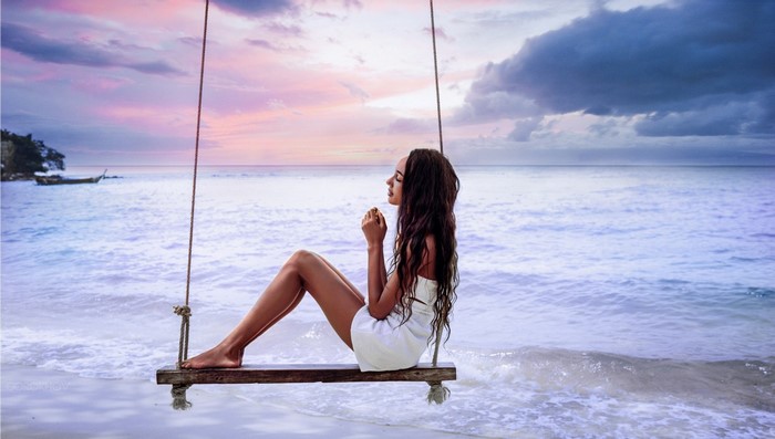 Woman sitting on a swing at the beach during sunset