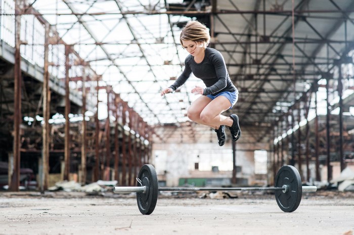 Woman jumping over barbell in abandoned warehouse