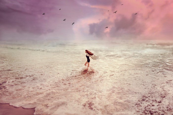 Woman walking in the ocean with birds flying overhead