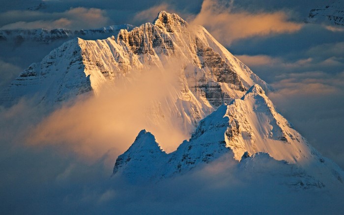 Snow-covered mountain peaks emerge from clouds at sunset
