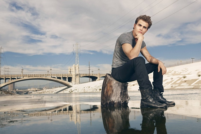 Paul Wesley sitting on a log by a river