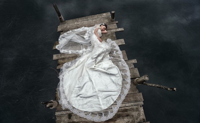 Bride in white dress lying on a wooden pier