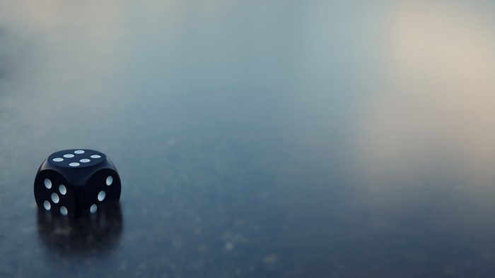Black die with white dots on a reflective surface