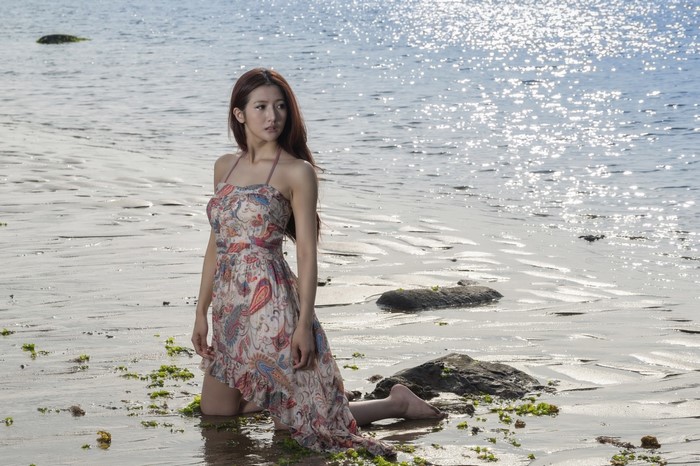 Woman in dress kneeling on a sandy beach by the sea