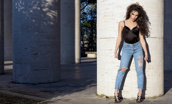 Woman in ripped jeans and black top posing by columns