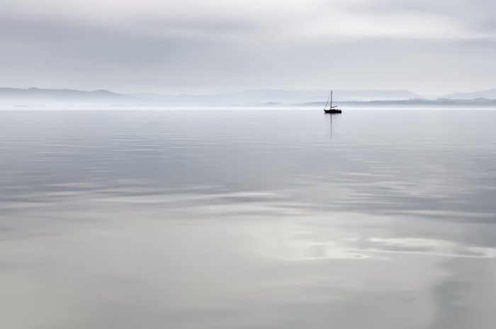 Sailboat on a calm lake with misty mountains