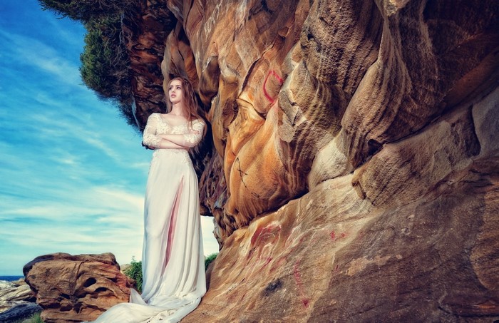 Woman in a white dress standing by a rock formation