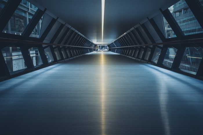 Modern glass and steel pedestrian tunnel with a lone figure