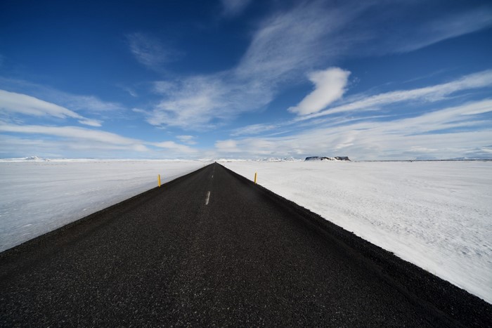 Asphalt road through a snowy landscape under a blue sky