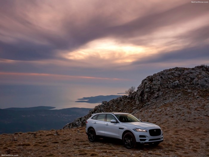 White Jaguar F-Pace SUV on a rocky mountain overlooking the sea at sunset