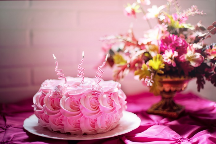 Pink birthday cake with candles and flowers