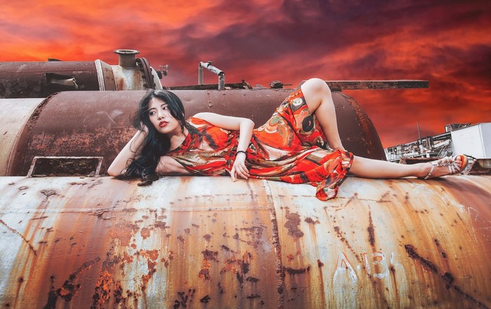 Woman in Red Dress Lying on Rusty Tank at Sunset