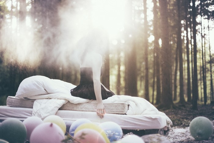 Woman in black dress on bed in forest with balloons
