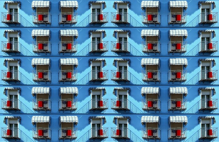 Pattern of blue building facade with balconies and red buckets