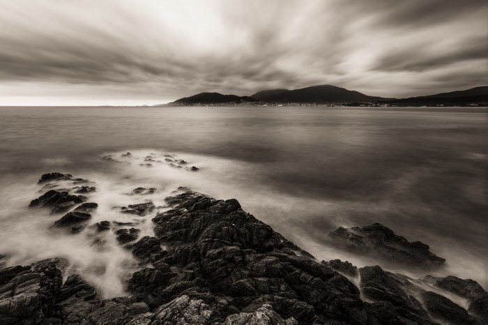 Monochrome seascape with rocky coast and distant mountains