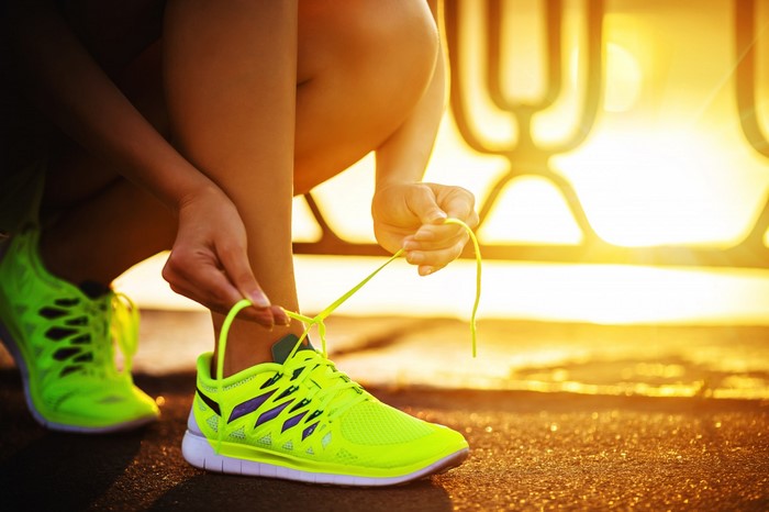 Person tying neon green running shoes at sunset