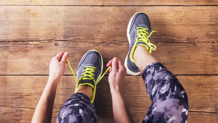 Person tying running shoes on wooden floor