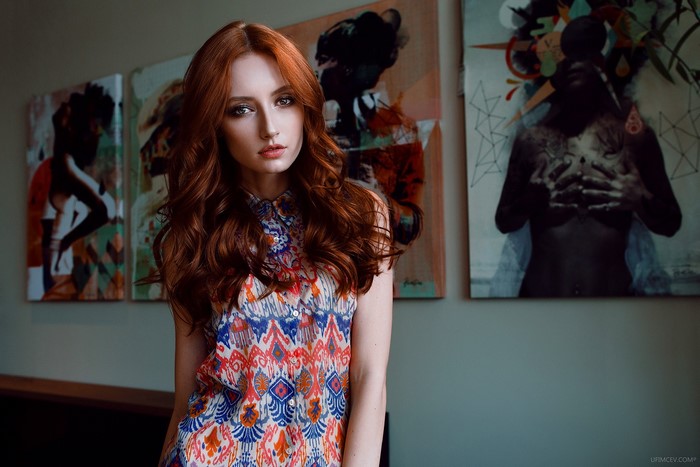 Redhead woman in colorful dress posing in front of art