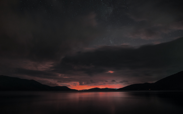 Dark lake at night with colorful clouds and stars