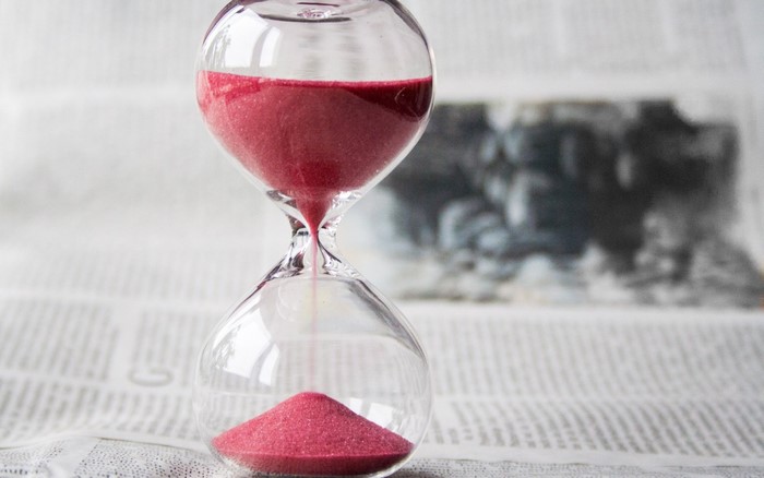 Hourglass with pink sand on a newspaper