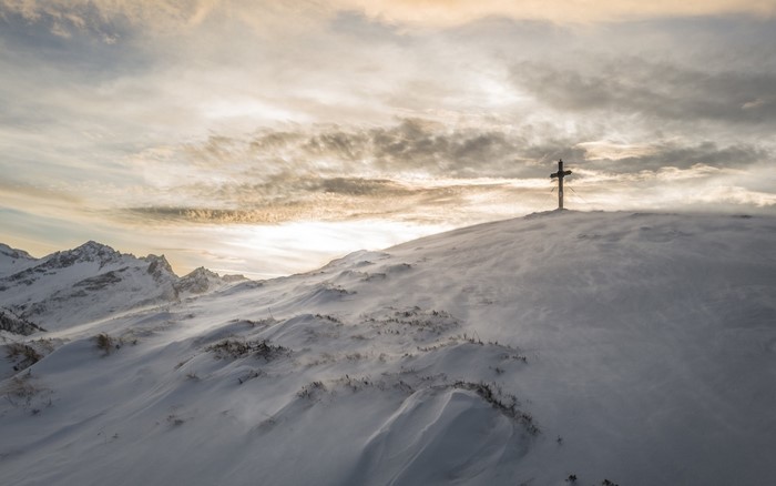 Cross on a snowy mountain peak at sunrise