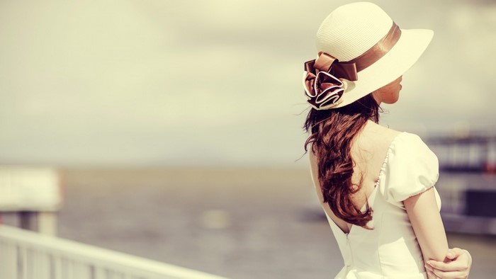 Woman in white dress and hat looking out at the water