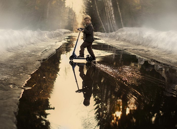 Boy on a scooter in a puddle with snow and trees