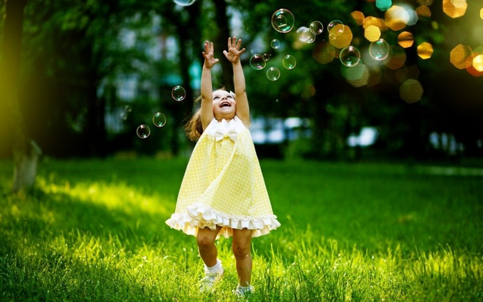 Little girl in yellow dress playing with bubbles in sunlight