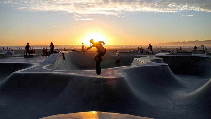 Skateboarder performs trick at sunset on beach skatepark