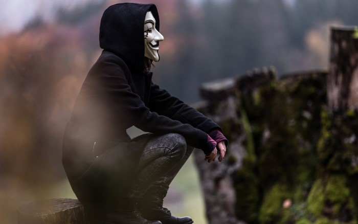 Person wearing Anonymous mask sitting outdoors