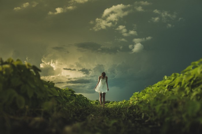 Woman in white dress walking in a field under stormy clouds