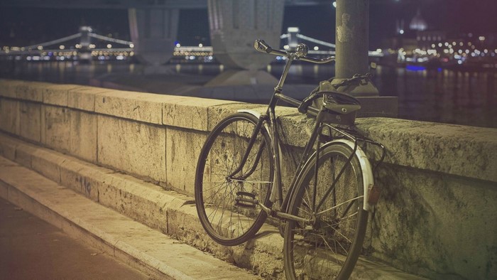 Bicycle parked by a stone wall at night with city lights in background