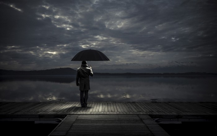 Man with umbrella on a pier at dusk