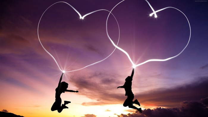 Couple drawing hearts in the sky at sunset