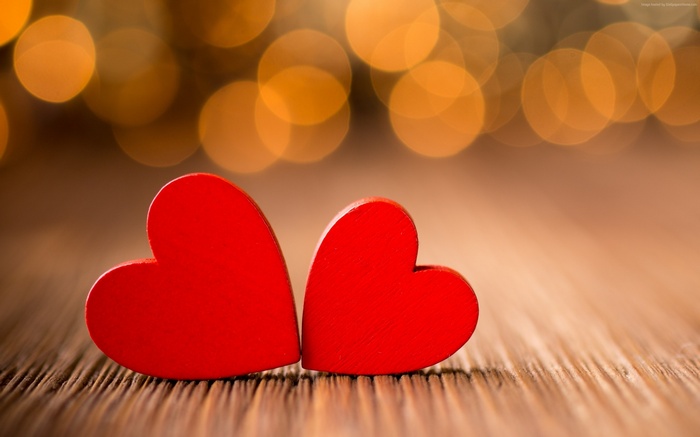 Two red hearts on a wooden surface with bokeh lights