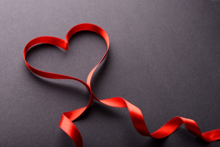 Red ribbon forming a heart shape on a dark background